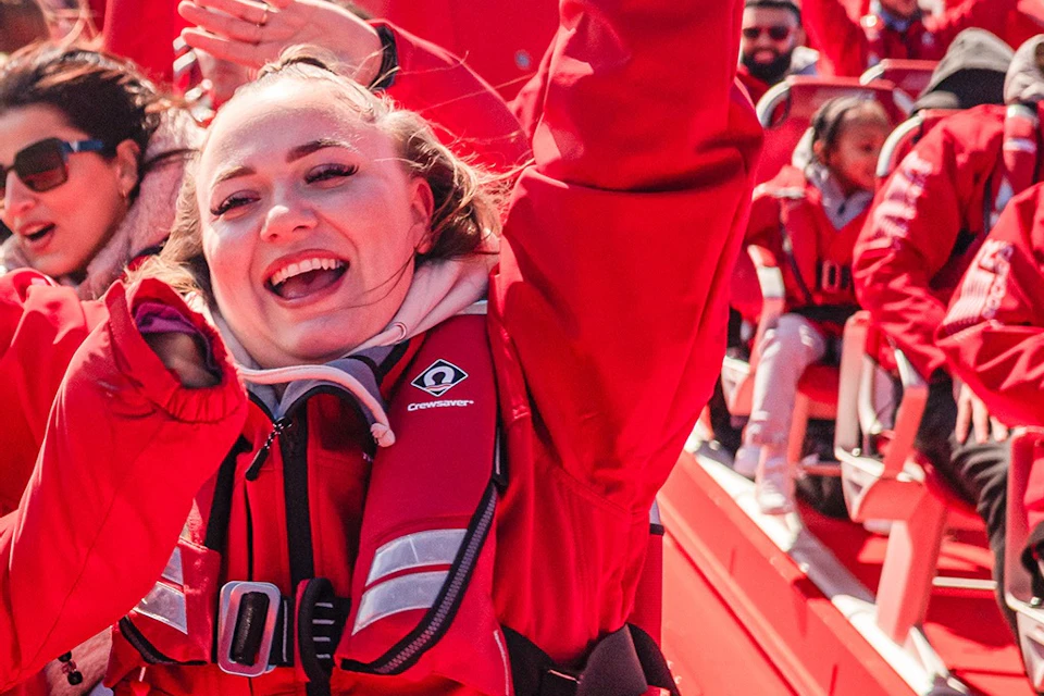People wearing red jackets smiling and raising their hands while enjoying a ride on a red speedboat.