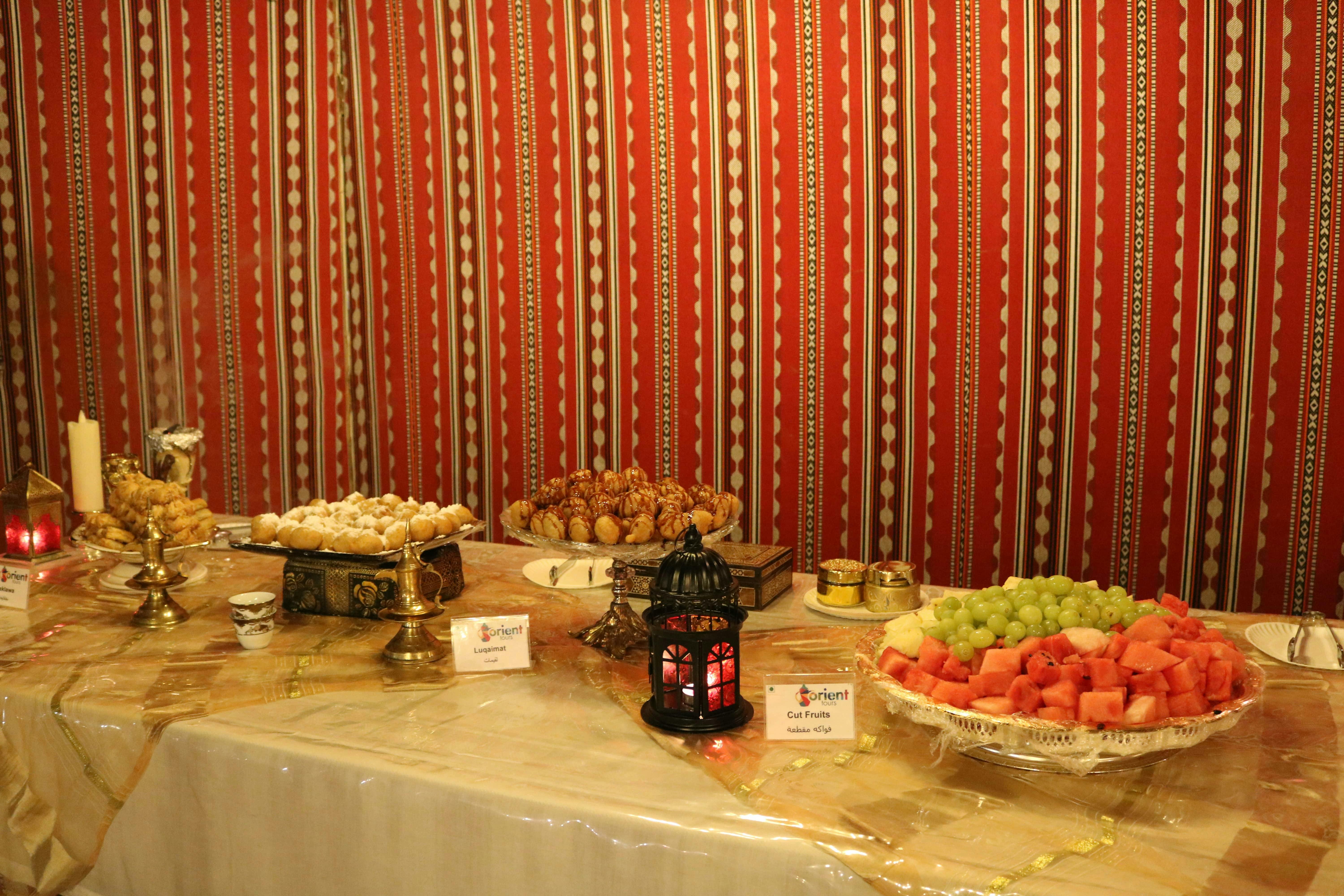 A buffet setup with assorted pastries, fresh fruits, and a lantern on a table against a red and white striped backdrop.
