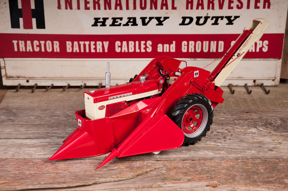 A red and white toy tractor is placed on a rustic wooden surface, with a vintage sign in the background reading “Heavy Duty.”