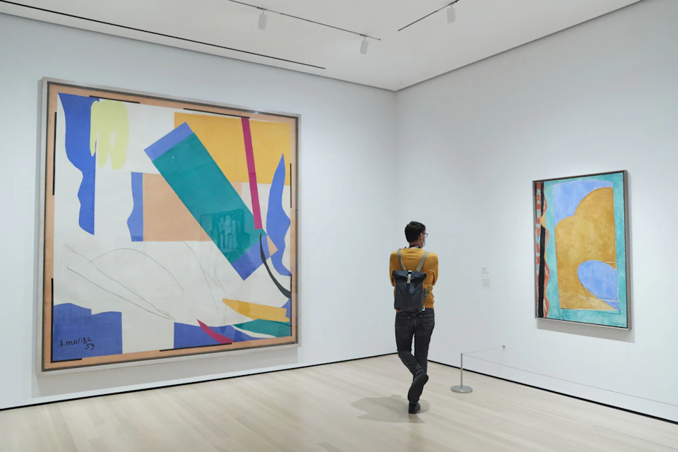 Person in a yellow sweater and backpack viewing large abstract paintings in a modern art gallery.