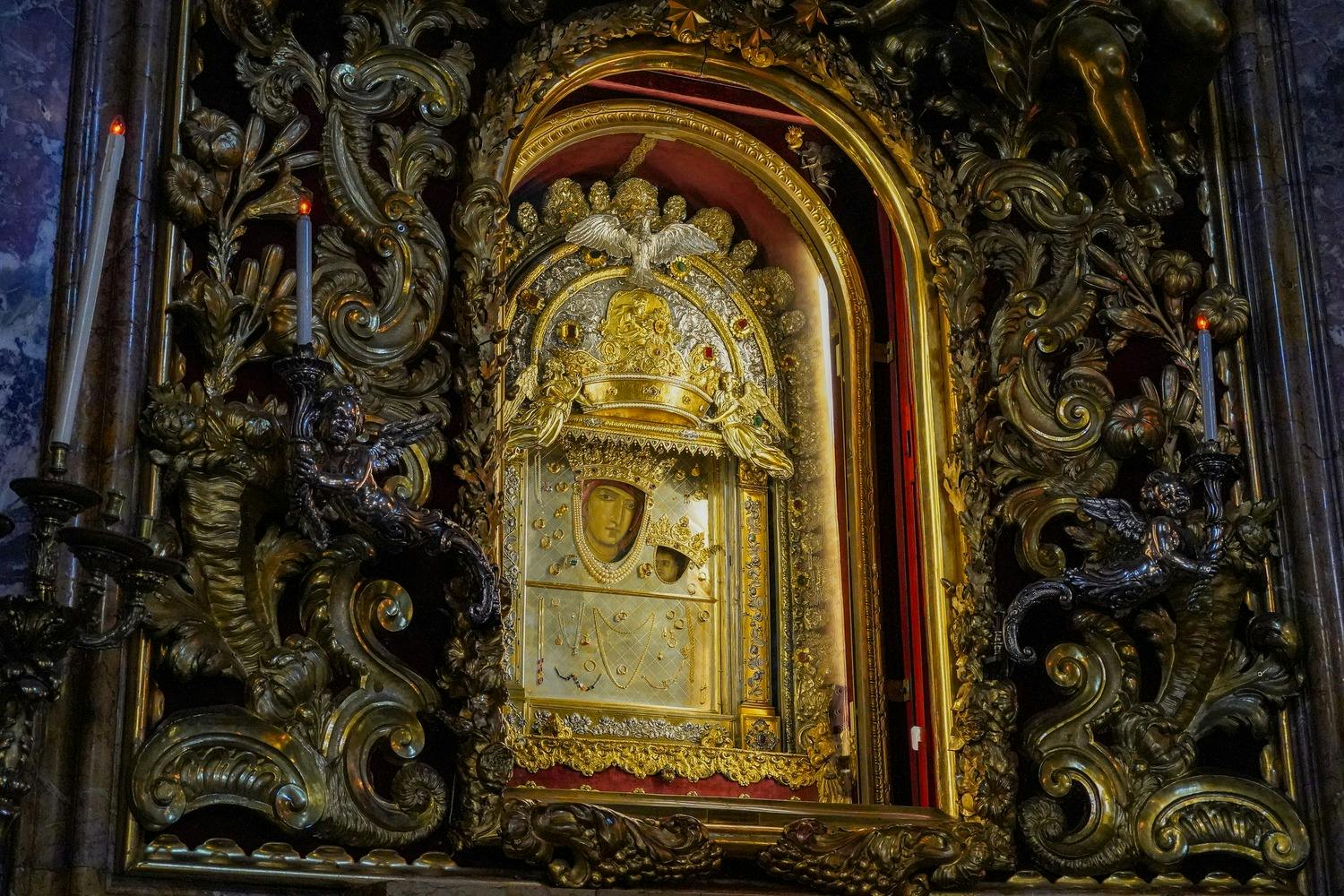 Ornate framed religious icon with gold embellishments and intricate carvings, surrounded by dark decorative elements.