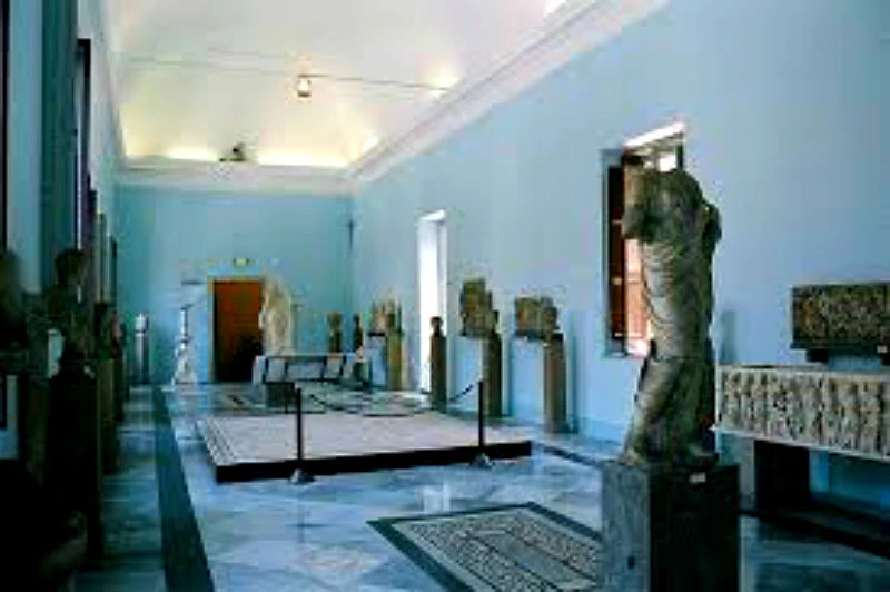 A museum gallery with blue walls, displaying various ancient sculptures and statues around the room.