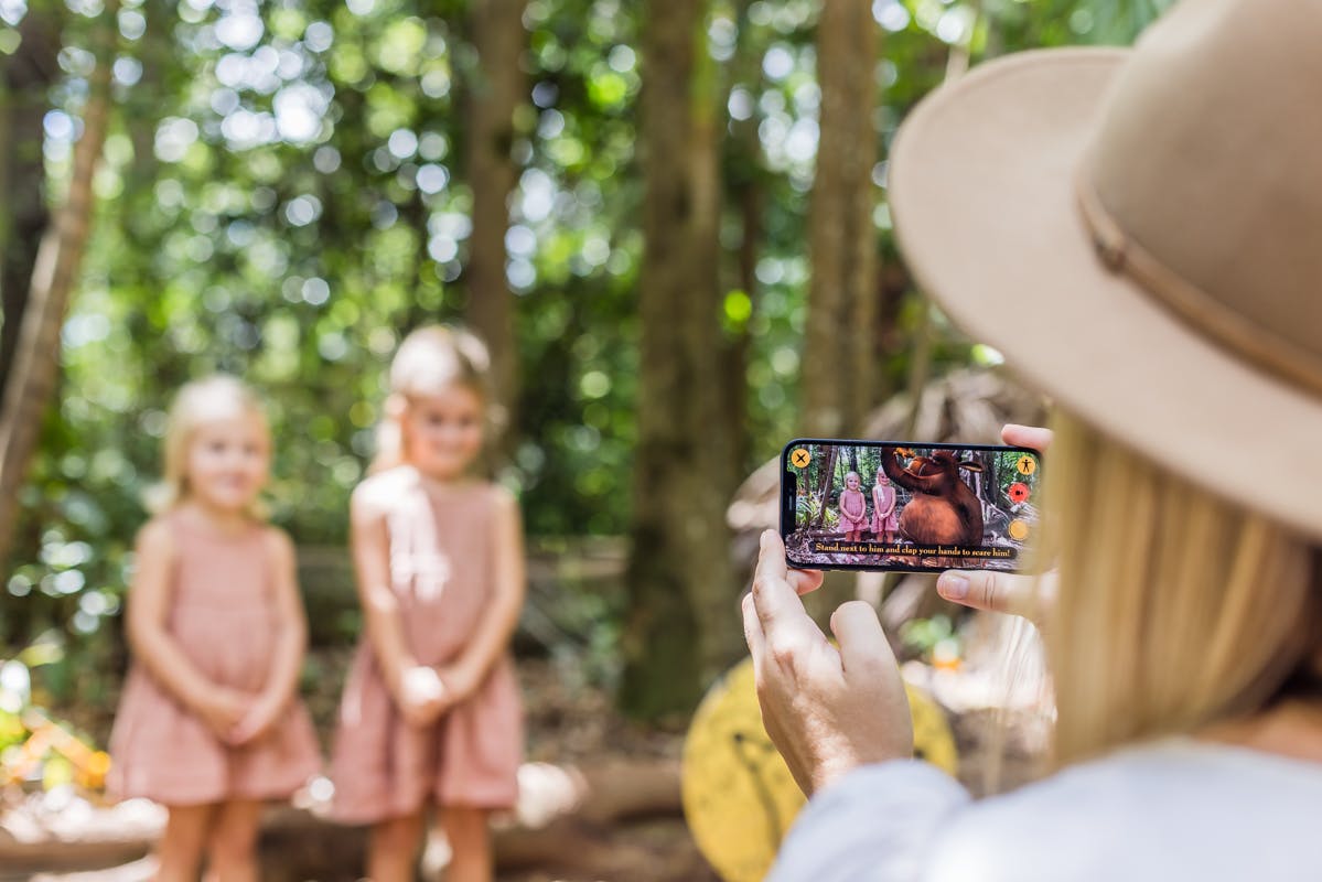 ある人がスマートフォンを使って、森の中に立っているピンク色のドレスを着た2人の若い女の子の写真を撮っています。