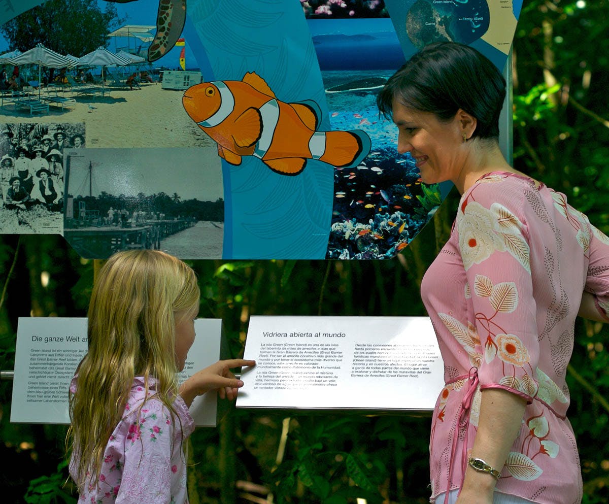 A woman and child in pink outfits read an informational display featuring an image of a clownfish in an outdoor setting.