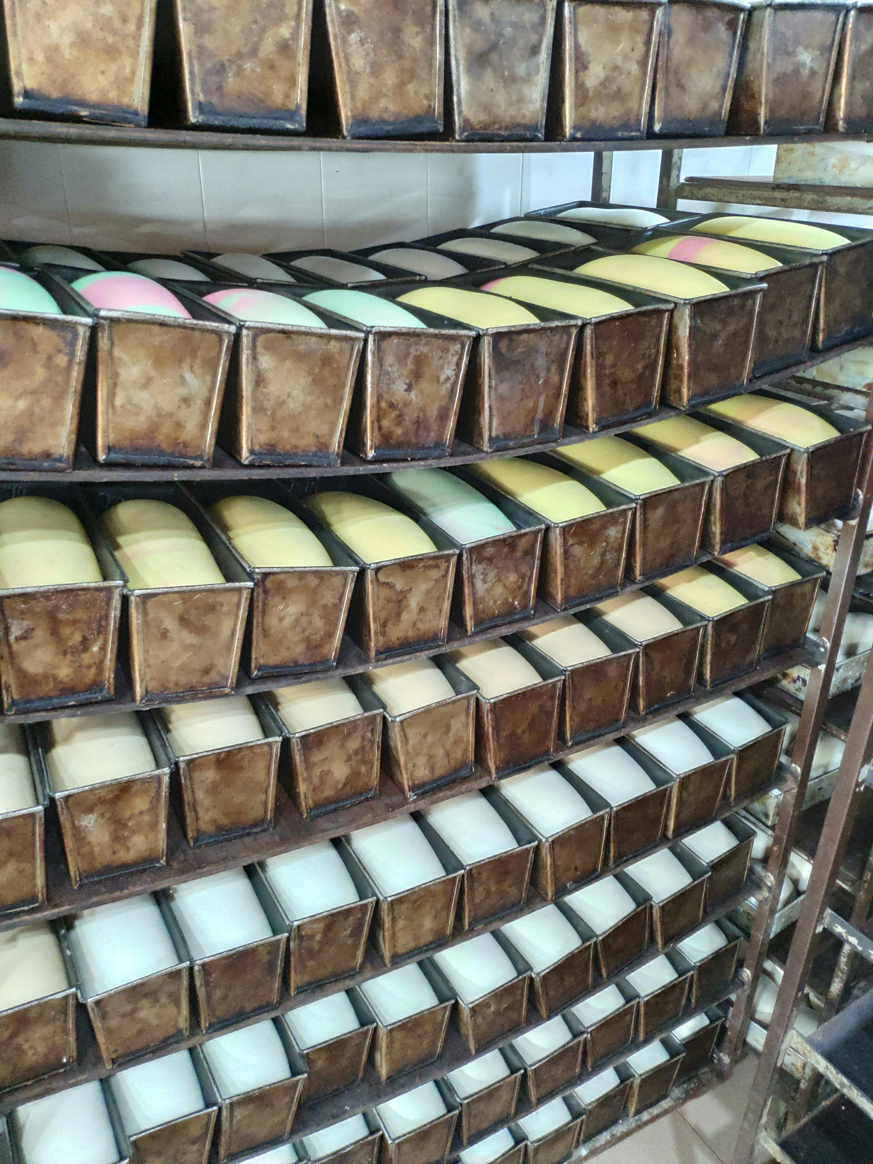 베이커리 랙에 다채로운 빵으로 채워진 금속 베이킹 팬이 줄지어 있습니다.