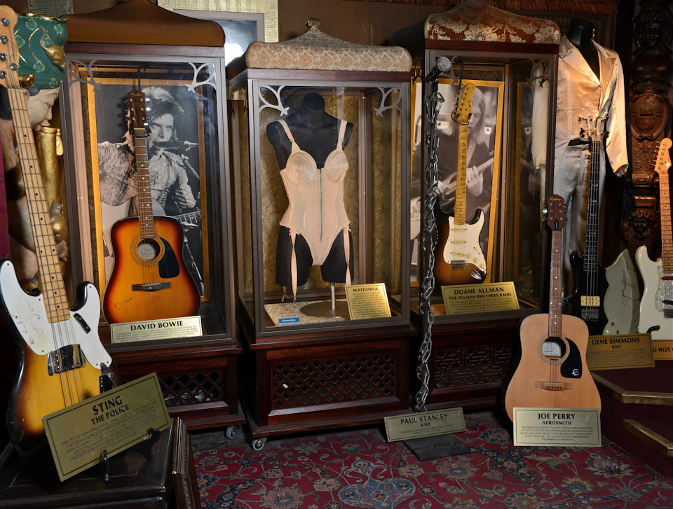 Display cases containing guitars and costumes, with name plaques for David Bowie, Duane Allman, Paul Stanley, and Joe Perry.