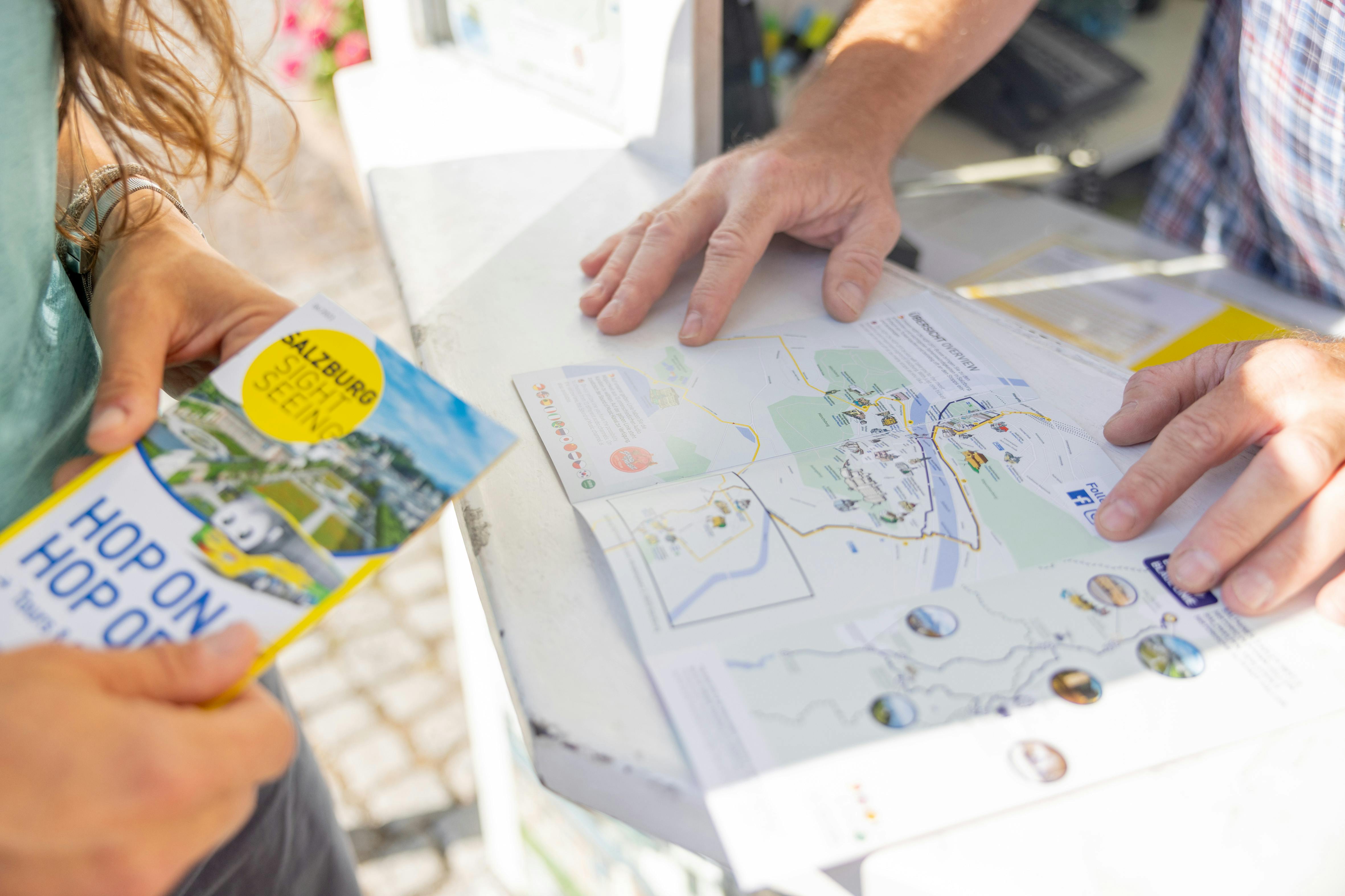 Dva lidé se dívají na mapu na pultu, jeden drží vyhlídkovou brožuru ze Salcburku.