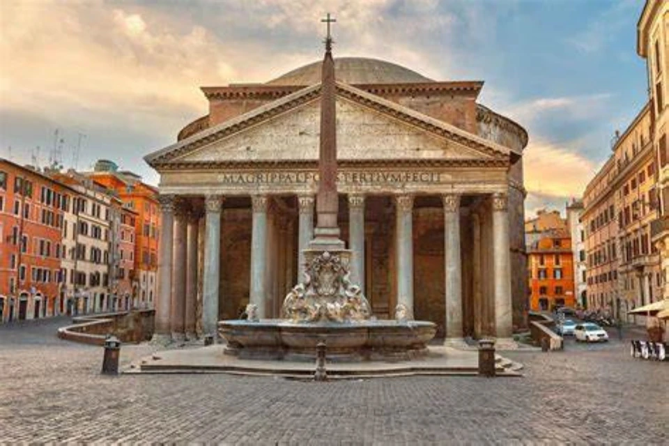 Front view of the Pantheon in Rome at sunset, with an obelisk and fountain in the foreground. Historic buildings surround the plaza.