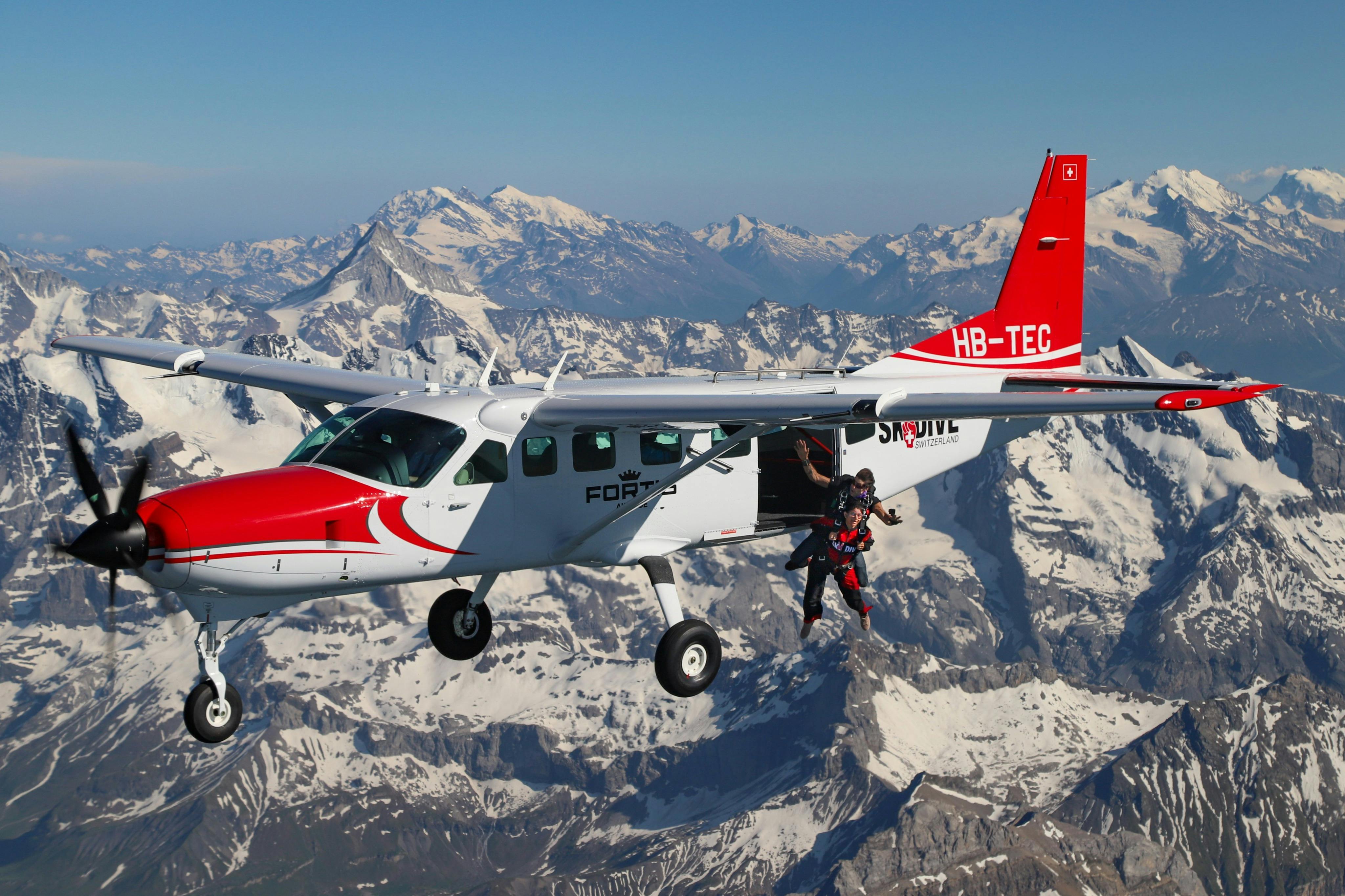 Skydivers jumping from a red and white airplane with a mountainous snowy landscape in the background.