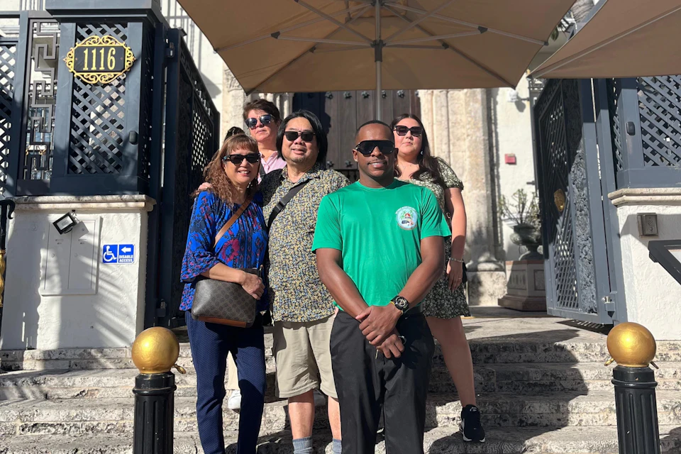 A tour guide poses with a group in front of the Versace Mansion.