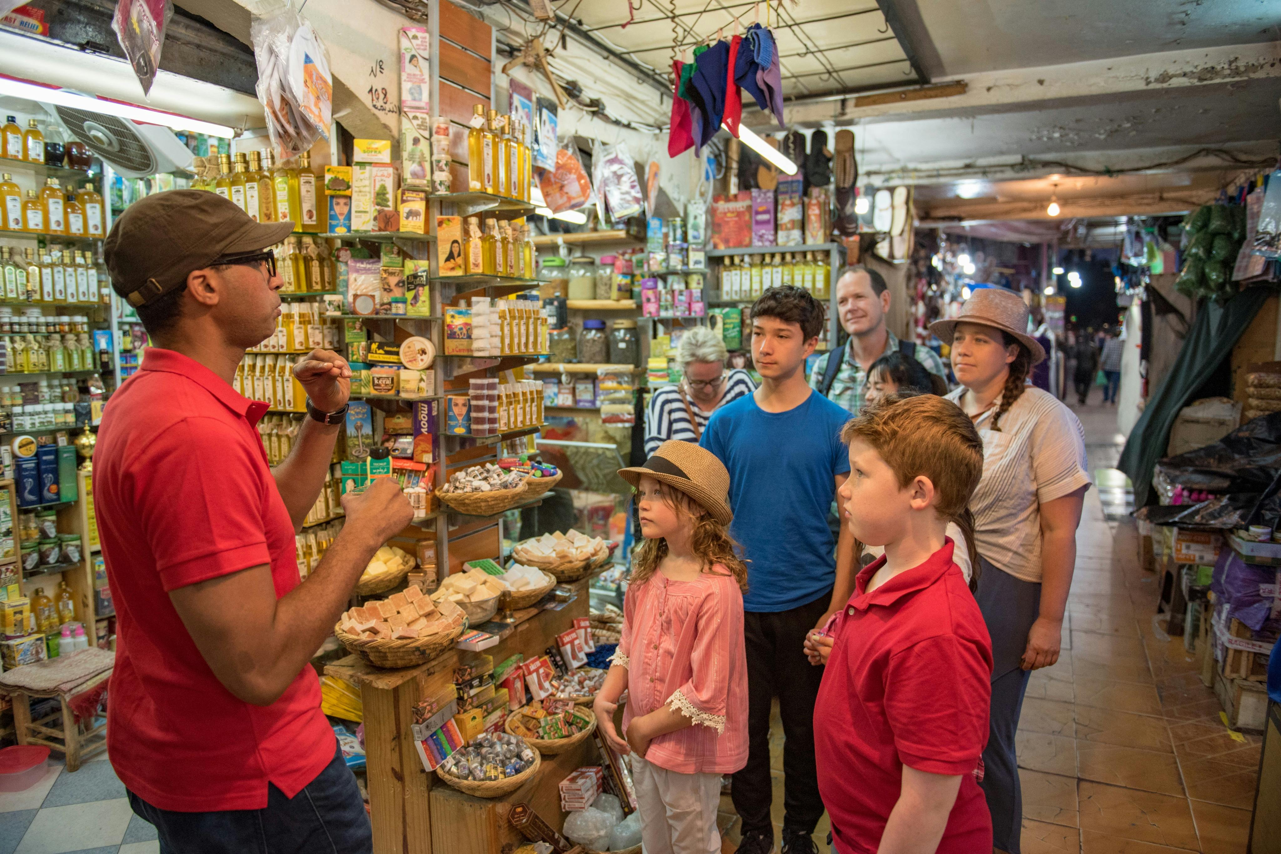 カラフルで混雑したマーケットショップで、ベンダーが話しかけてくると、子供たちを含むグループの人々が注意深く立っています。