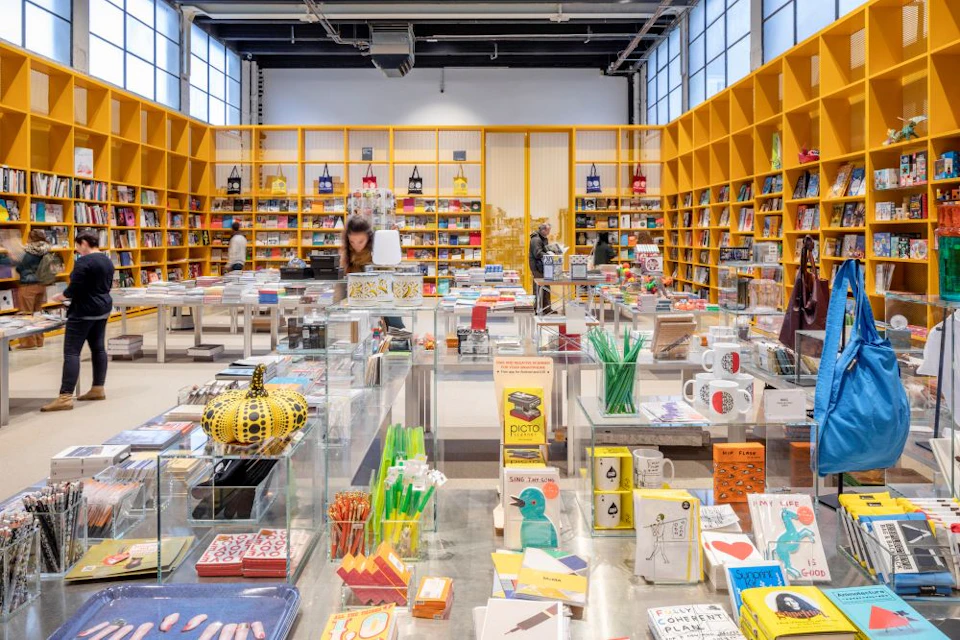 A brightly lit store featuring shelves of books and colorful items, with customers browsing and products displayed on tables.