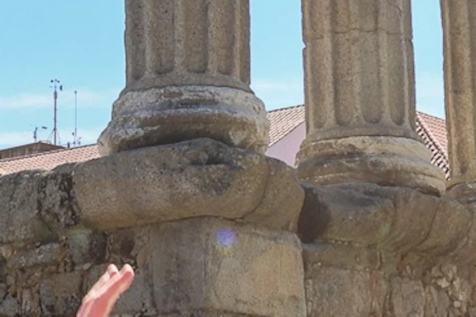 A man in a red polo shirt explains a site to a woman near ancient stone columns under a clear blue sky.