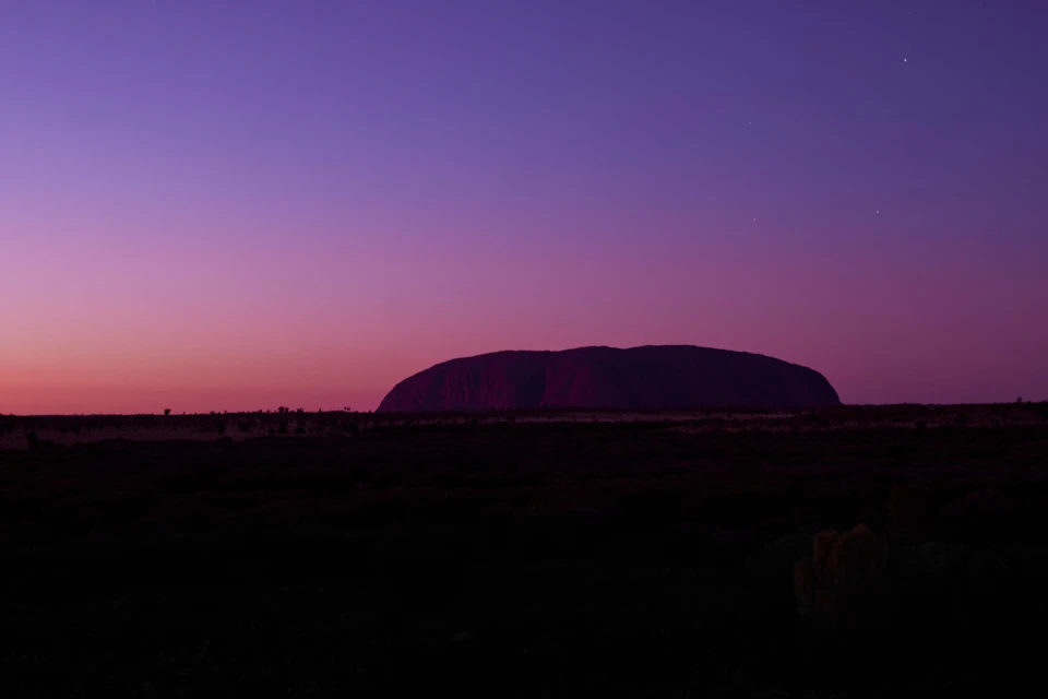 Silhouette of a large rock formation under a gradient sky transitioning from pink to purple at sunset.