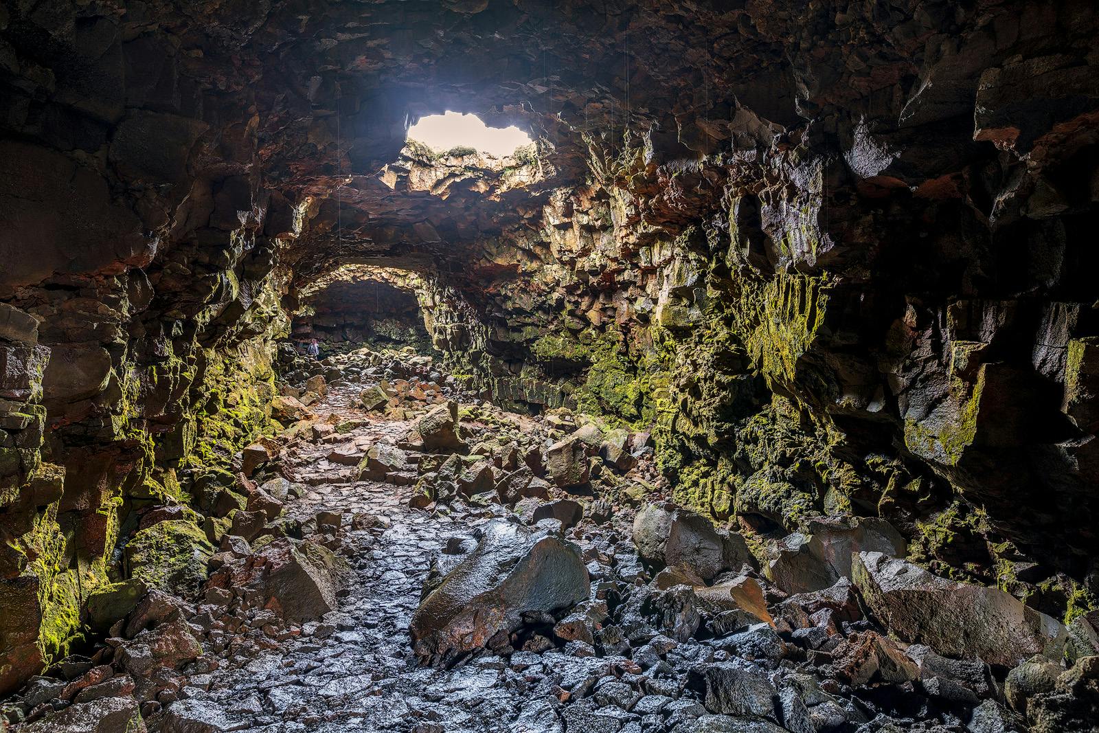 Una grotta rocciosa e ricoperta di muschio con una vista sul cielo attraverso una grande apertura in cima.