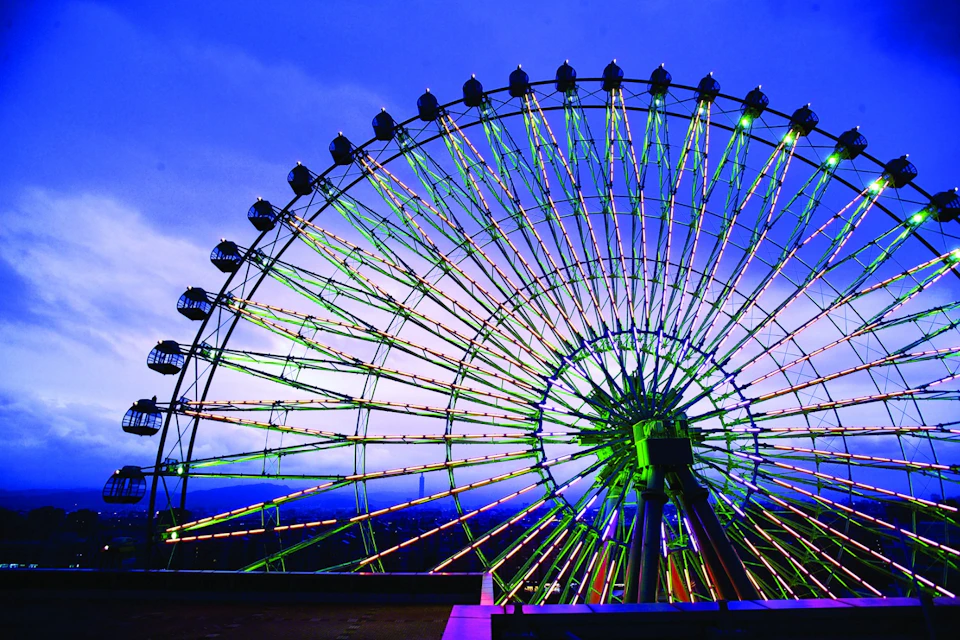 A brightly lit ferris wheel with colorful lights against a twilight sky.