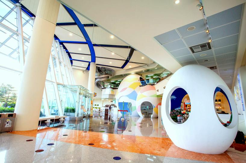 A colorful and modern indoor space with artistic structures, glass walls, and a display featuring a model cityscape.