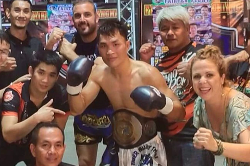 A group of people posing together indoors, with a Muay Thai fighter in the center holding a championship belt.