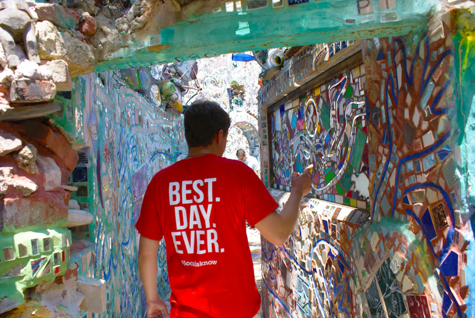 Person in a red shirt with "BEST. DAY. EVER." navigating a narrow, mosaic-tiled corridor.