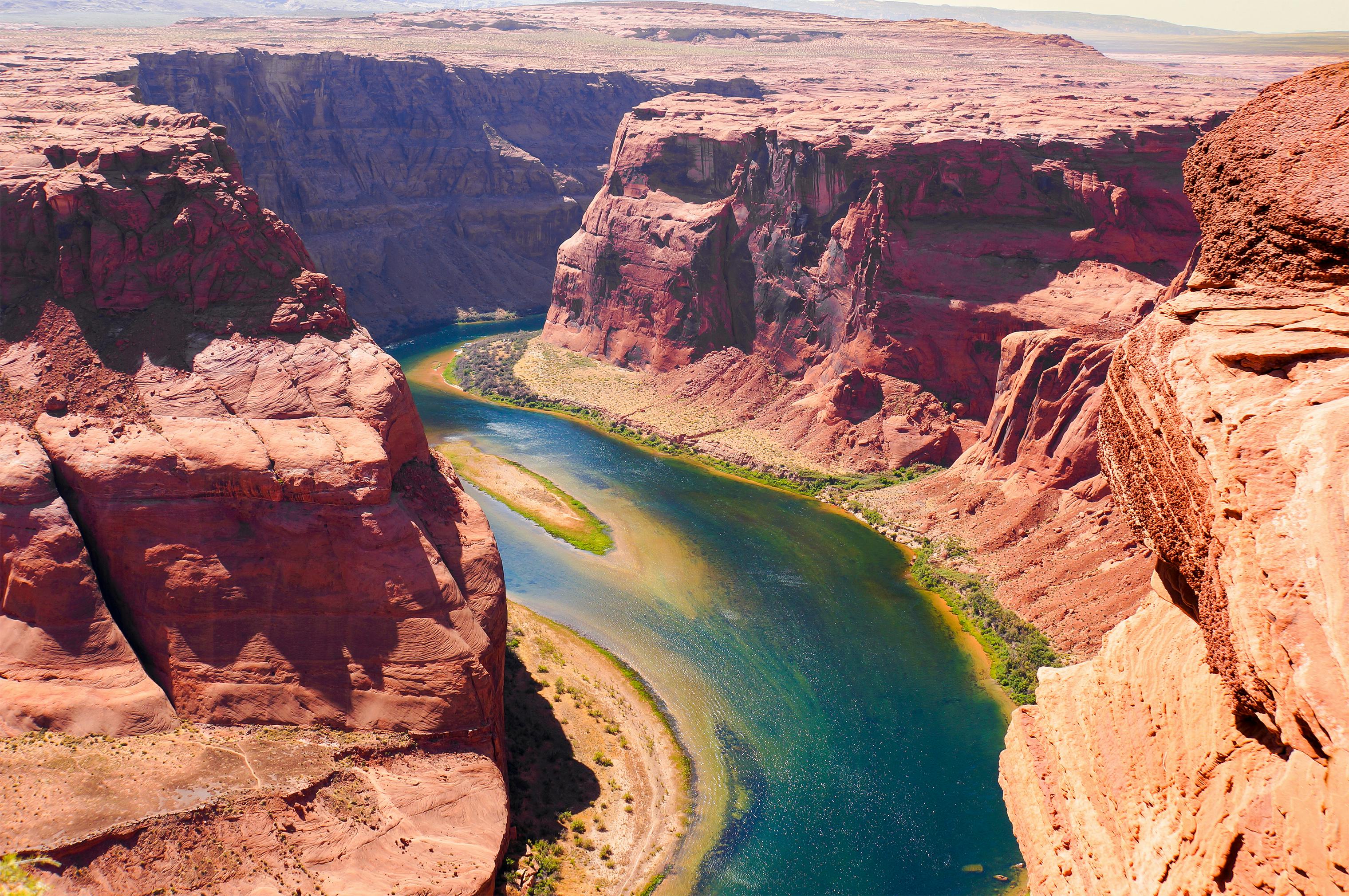 Aerial view of a winding river through a deep, reddish canyon with steep cliff walls and sparse vegetation.