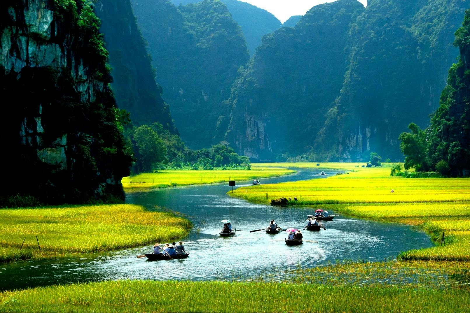 높고 험준한 산으로 둘러싸인 울창하고 푸른 계곡을 따라 흐르는 강에서 사람들이 노를 젓고 있는 여러 보트.