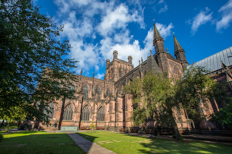 Gothic-style cathedral with tall spires, ornate windows, and lush greenery in the foreground under a bright blue sky.