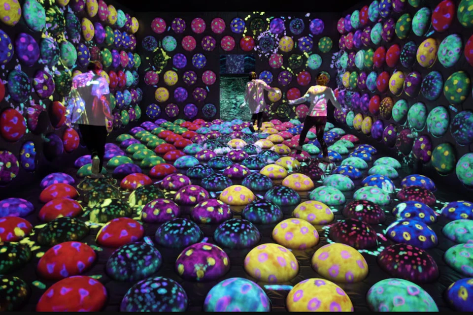 Three people interact in a colorful room filled with glowing, patterned spheres and projections on the walls and floor.