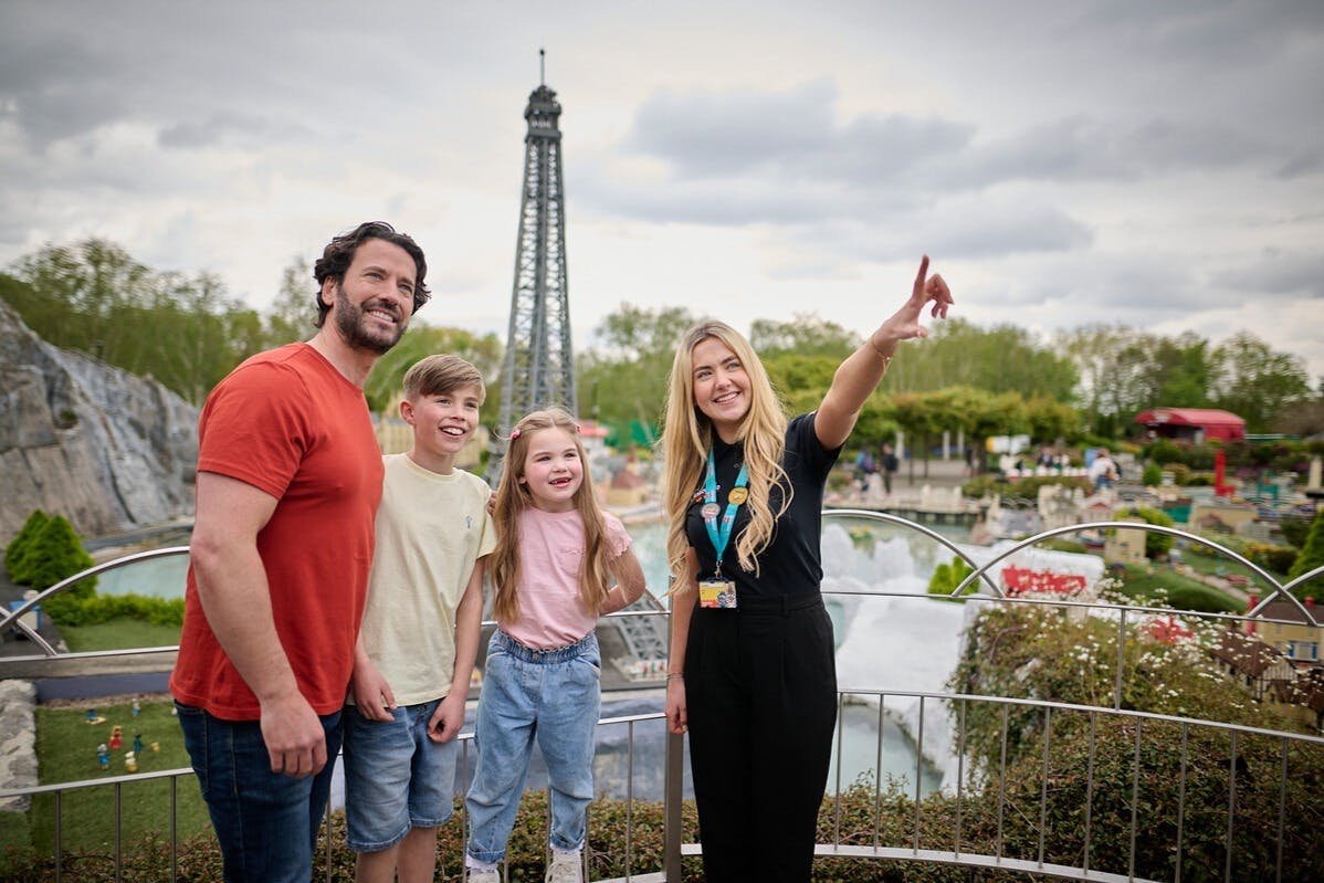 Um grupo de quatro pessoas, incluindo duas crianças e dois adultos, sorriem junto a uma réplica de um marco histórico num parque.