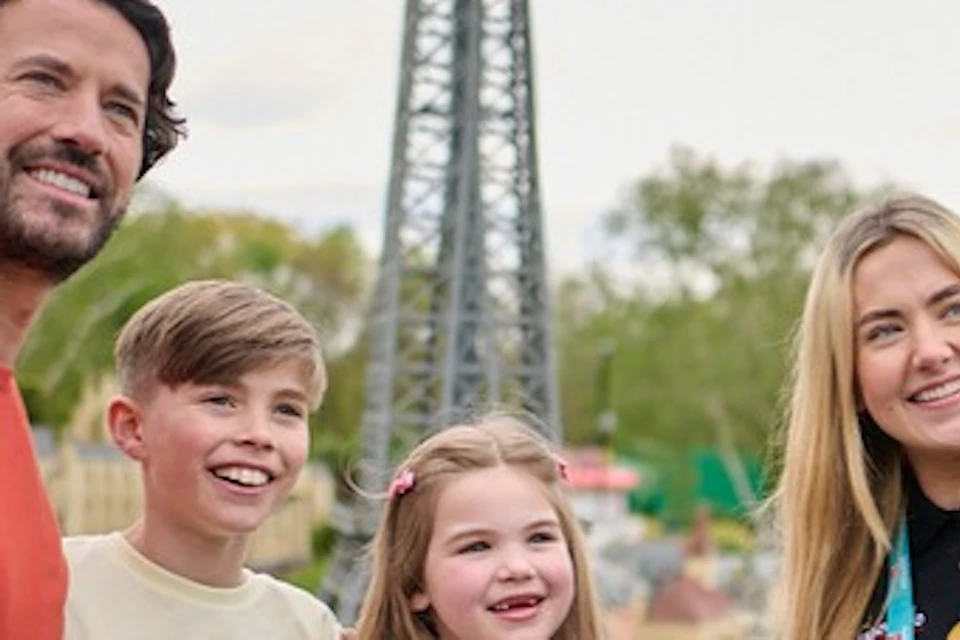 A group of four people, including two children and two adults, stand smiling near a landmark replica in a park setting.