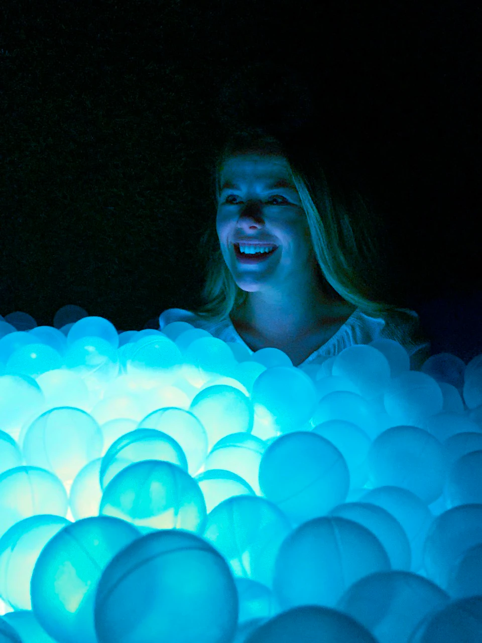 A person smiling in a dark environment surrounded by glowing blue spheres, creating a luminous, ethereal ambiance.