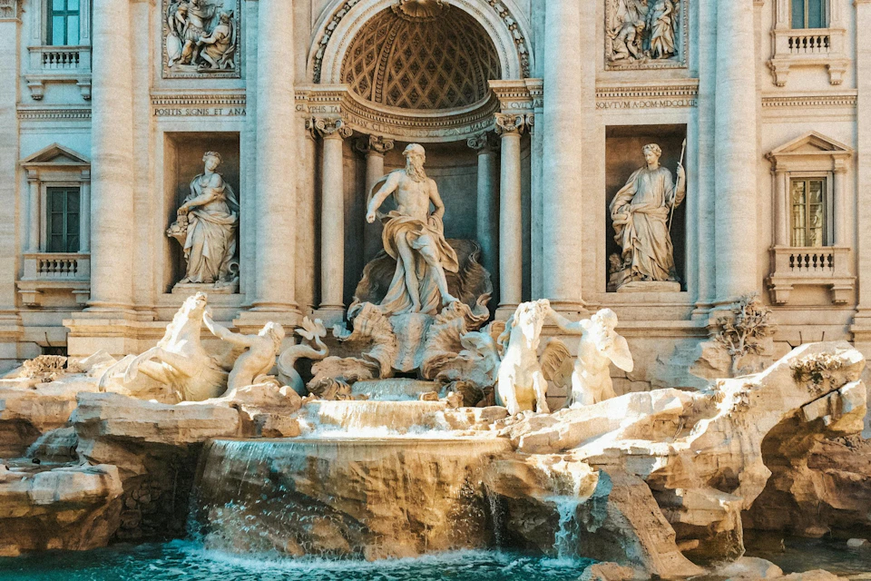 A grand sculptural fountain featuring statues and flowing water, set against an ornate architectural backdrop.