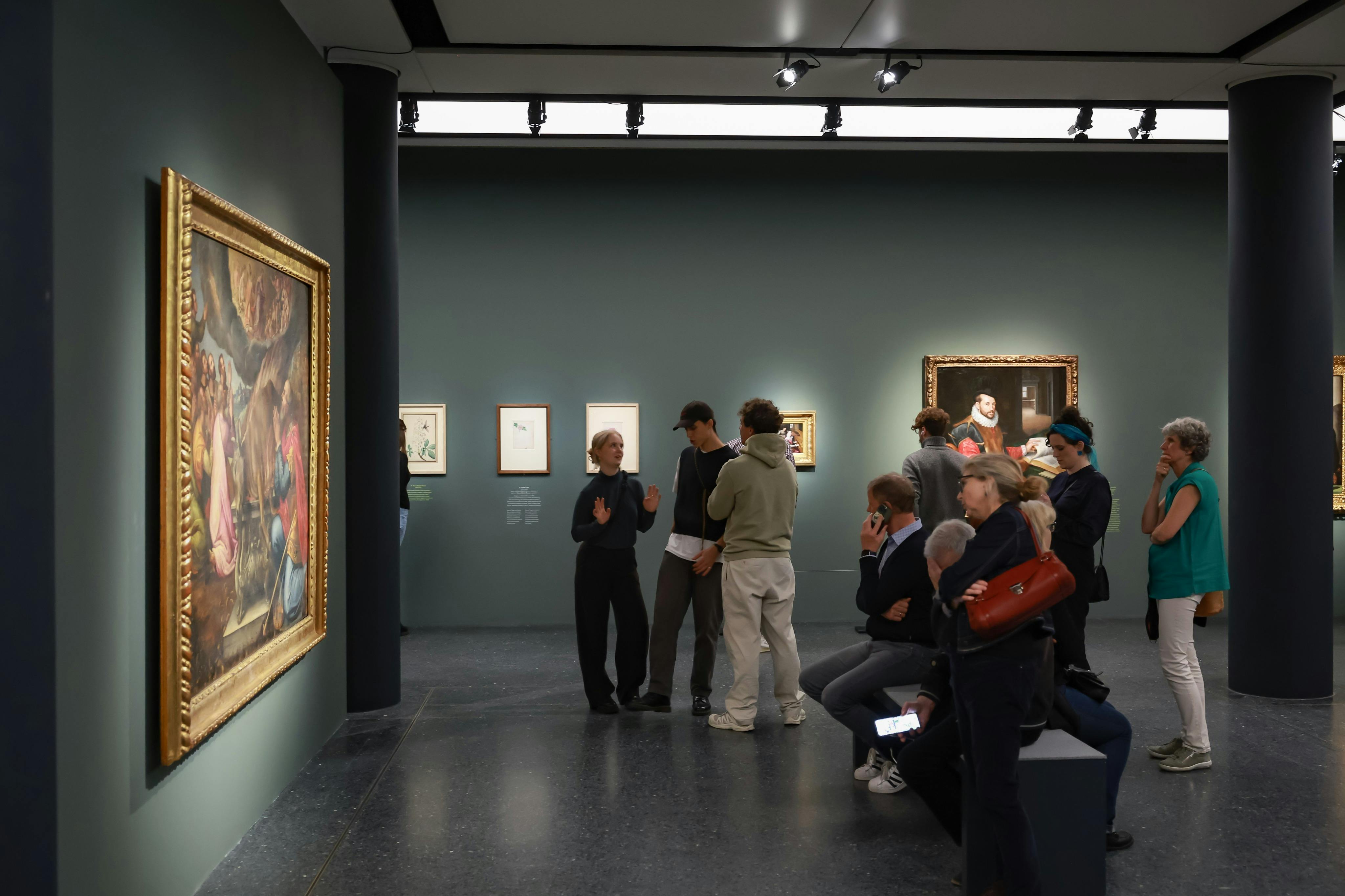 미술관에서 벽에 걸린 그림을 보며 앉거나 서서 이야기를 나누는 사람들.