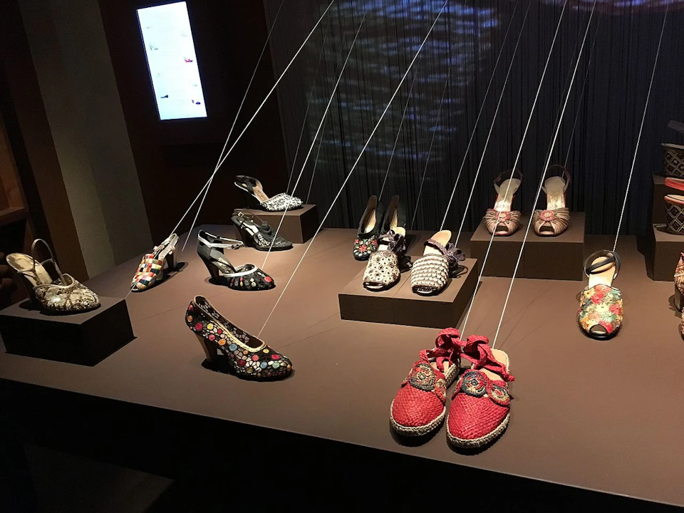 A display of various designer shoes, suspended by strings, showcased on elevated platforms in a dimly lit room.