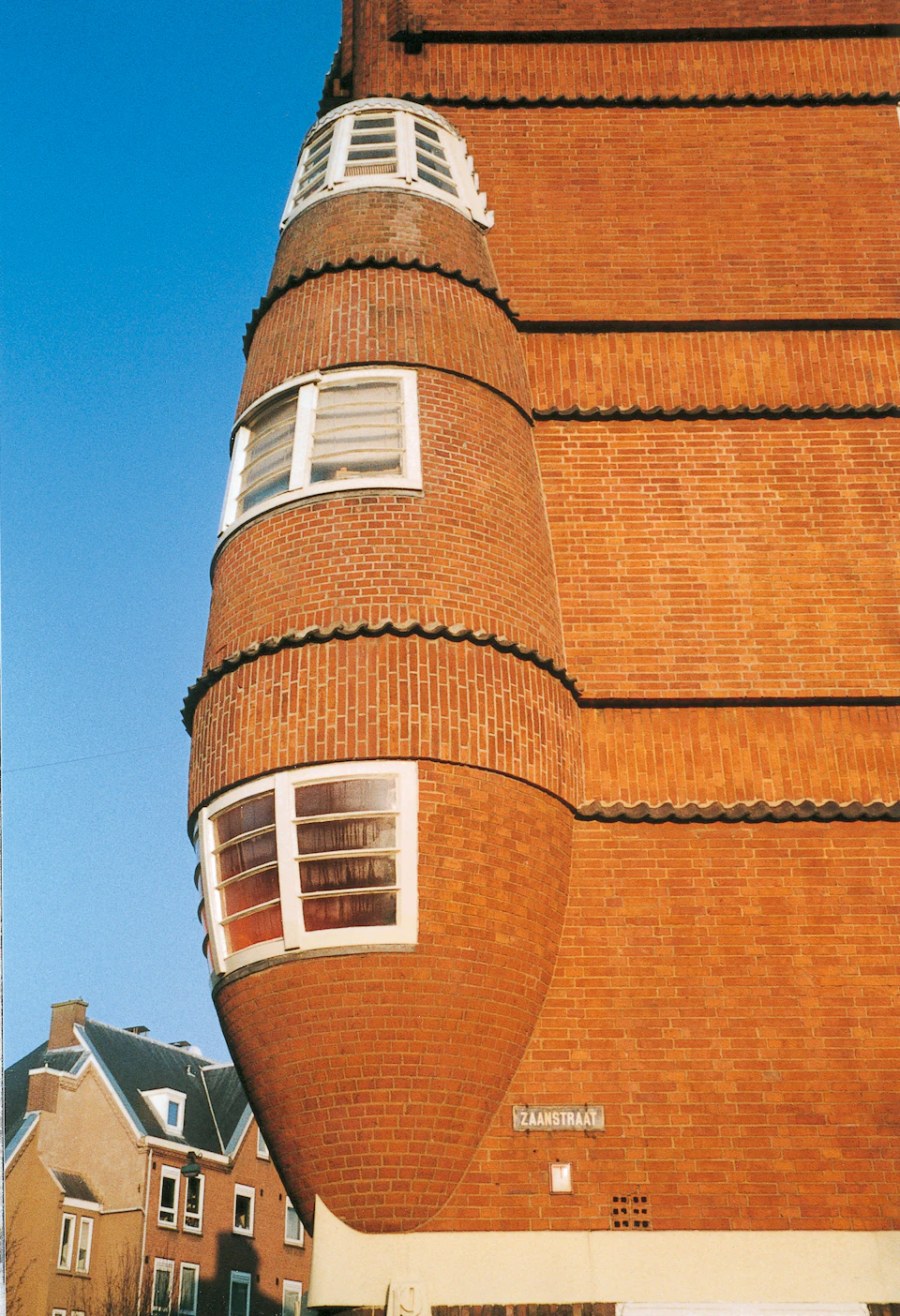 A unique brick building with protruding rounded sections featuring white-framed windows, set against a clear blue sky.