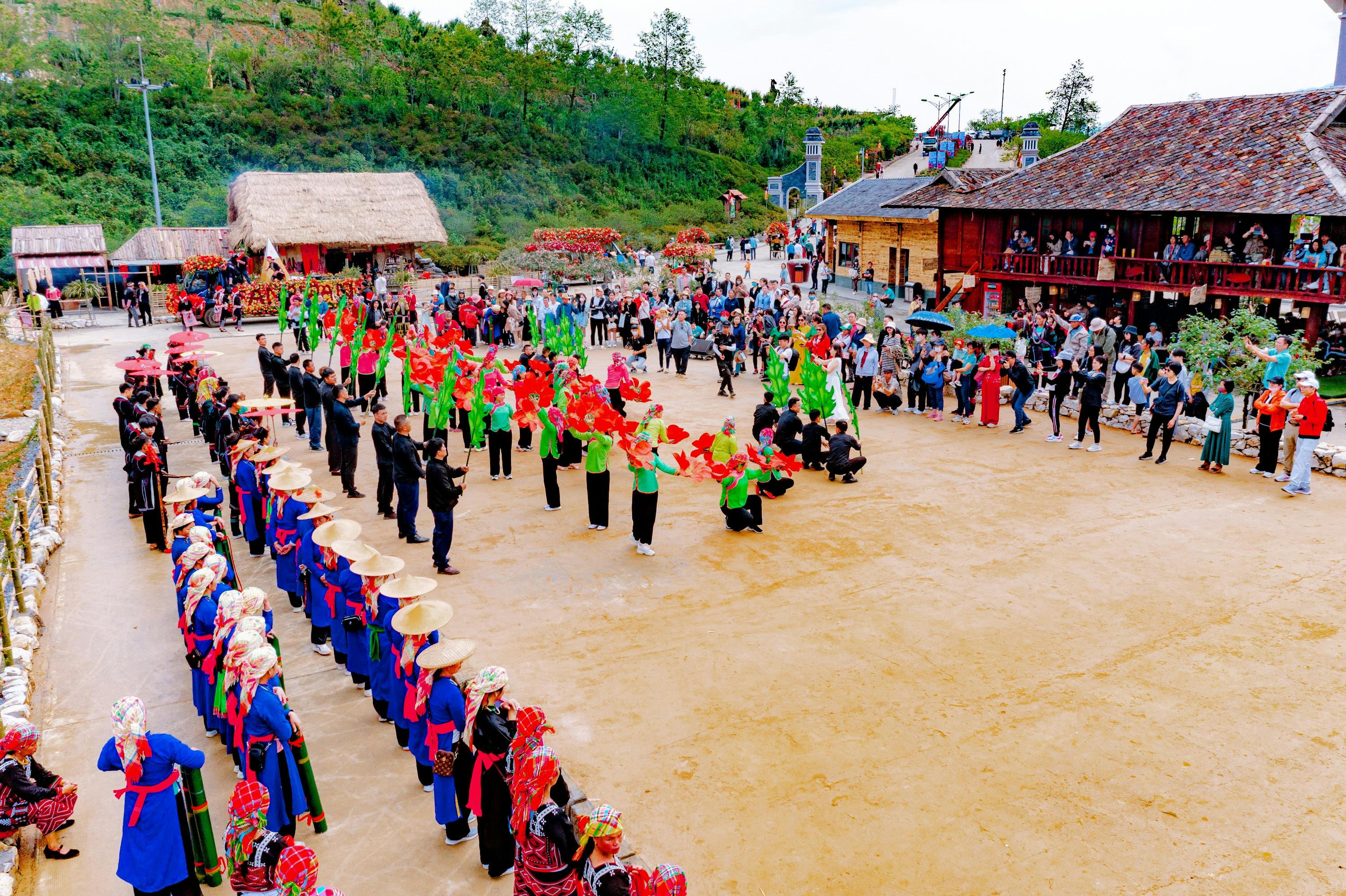 A vibrant outdoor cultural performance with participants in colorful traditional attire, surrounded by an audience in a village setting.