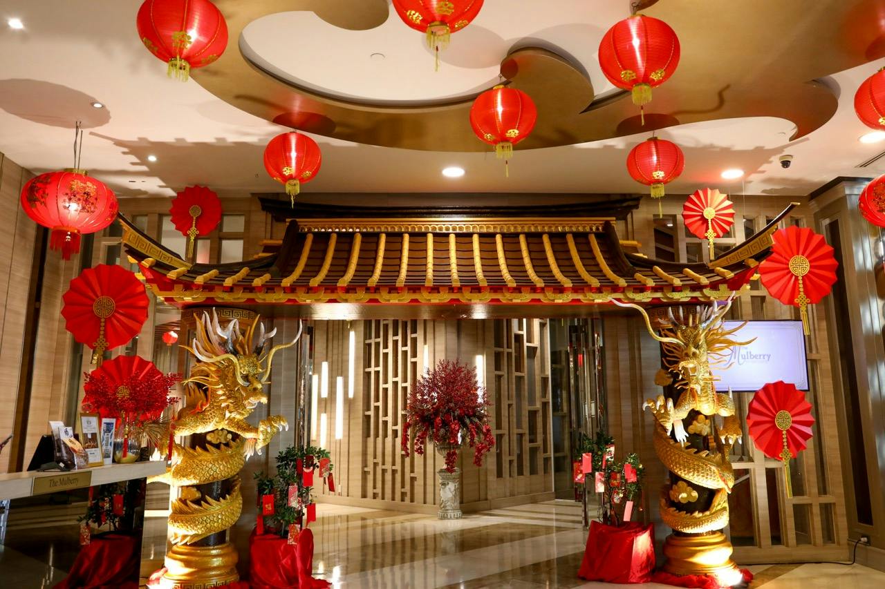 A decorative setup with red lanterns, golden dragons, and a traditional-style roof, celebrating a festive occasion indoors.