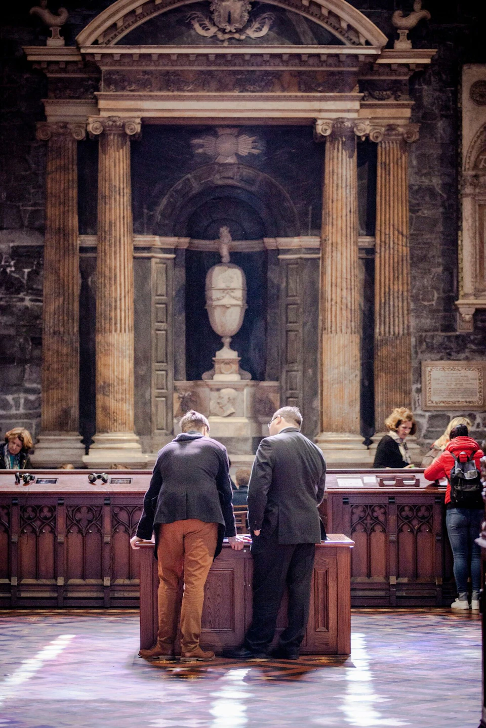 Several people observe artifacts inside a historical building with tall columns and a central statue.