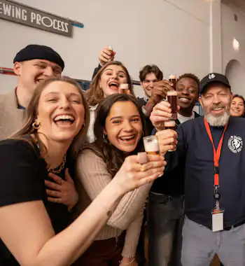Un grupo de personas sonriendo y sujetando vasos pequeños en un brindis de celebración en un ambiente interior.
