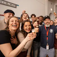 Un grup de persones somrient i sostenint petites copes juntes en un brindis de celebració en un entorn interior.