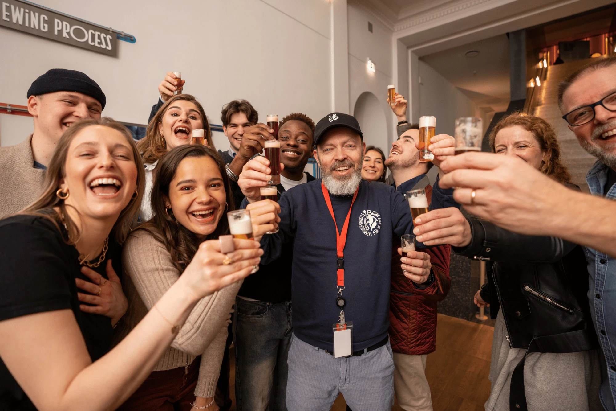 A group of people smiling and holding small glasses together in a celebratory toast in an indoor setting.
