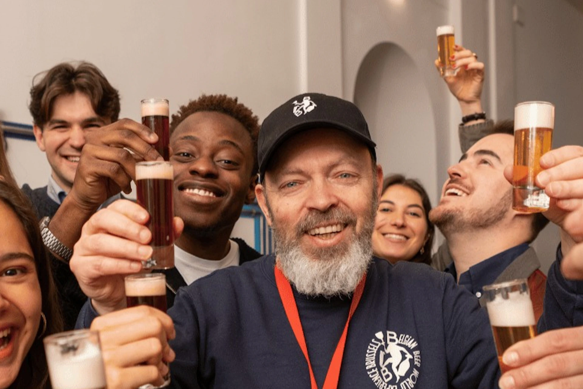 A group of people smiling and holding small glasses together in a celebratory toast in an indoor setting.