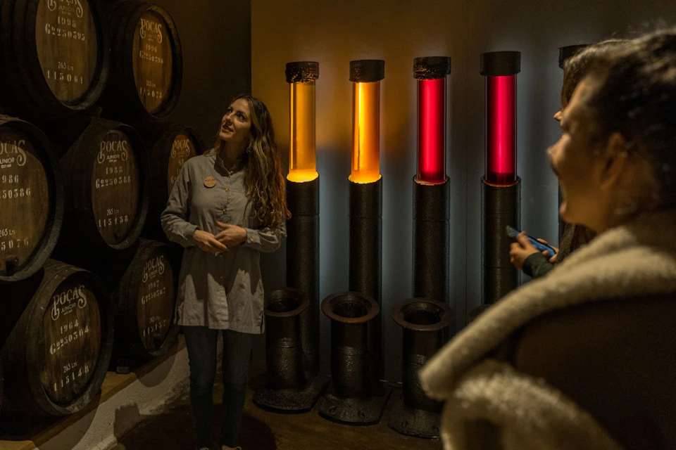 A guide stands near illuminated columns of colored liquid in an exhibit room, with barrels visible in the background.