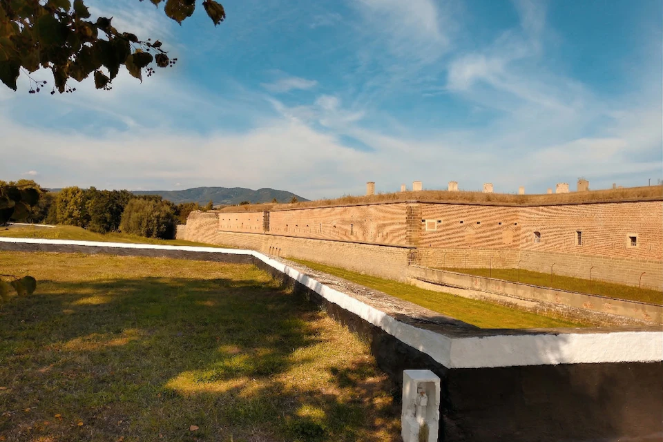 A brick wall surrounds a grassy area with a blue sky and mountains in the background.