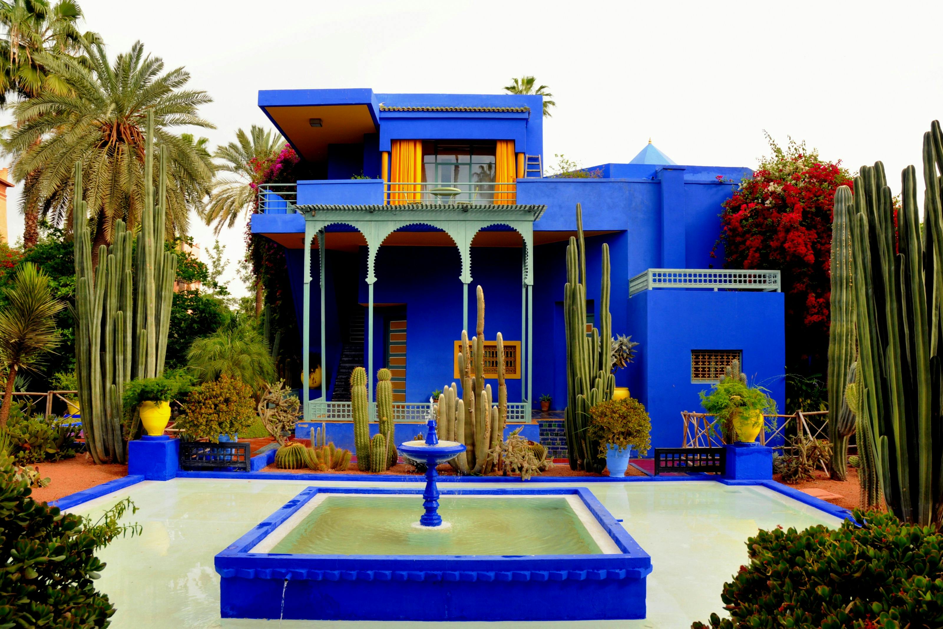 A striking blue building with arched details, surrounded by cacti and greenery, featuring a fountain in the foreground.