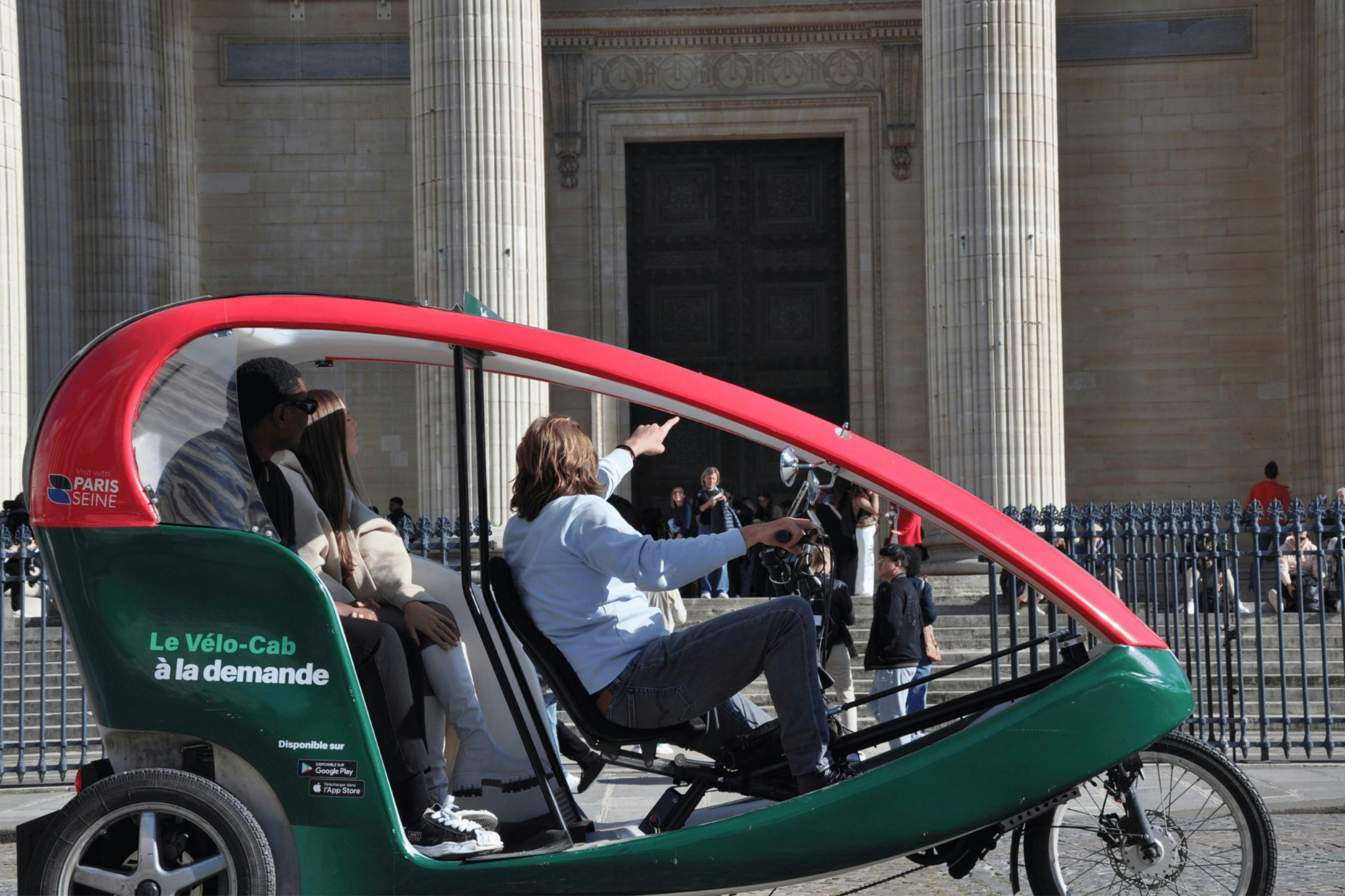 A rickshaw driver points out a landmark to two passengers in front of a large building with tall columns.