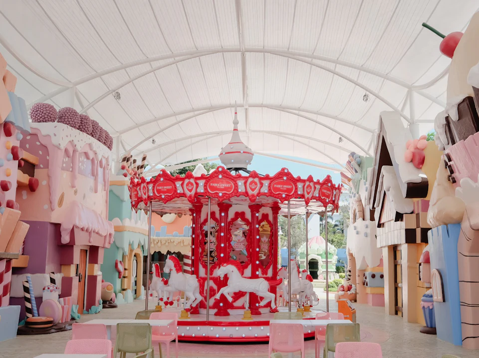 A brightly colored carousel with red and white details under a large canopy, surrounded by whimsical buildings.