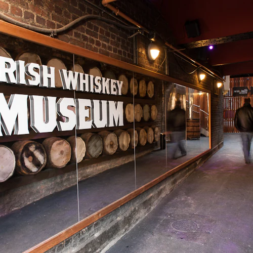 Svagt upplyst hall med whiskytunnor på båda sidor och en skylt där det står "Irish Whiskey Museum". En person går in i fjärran.