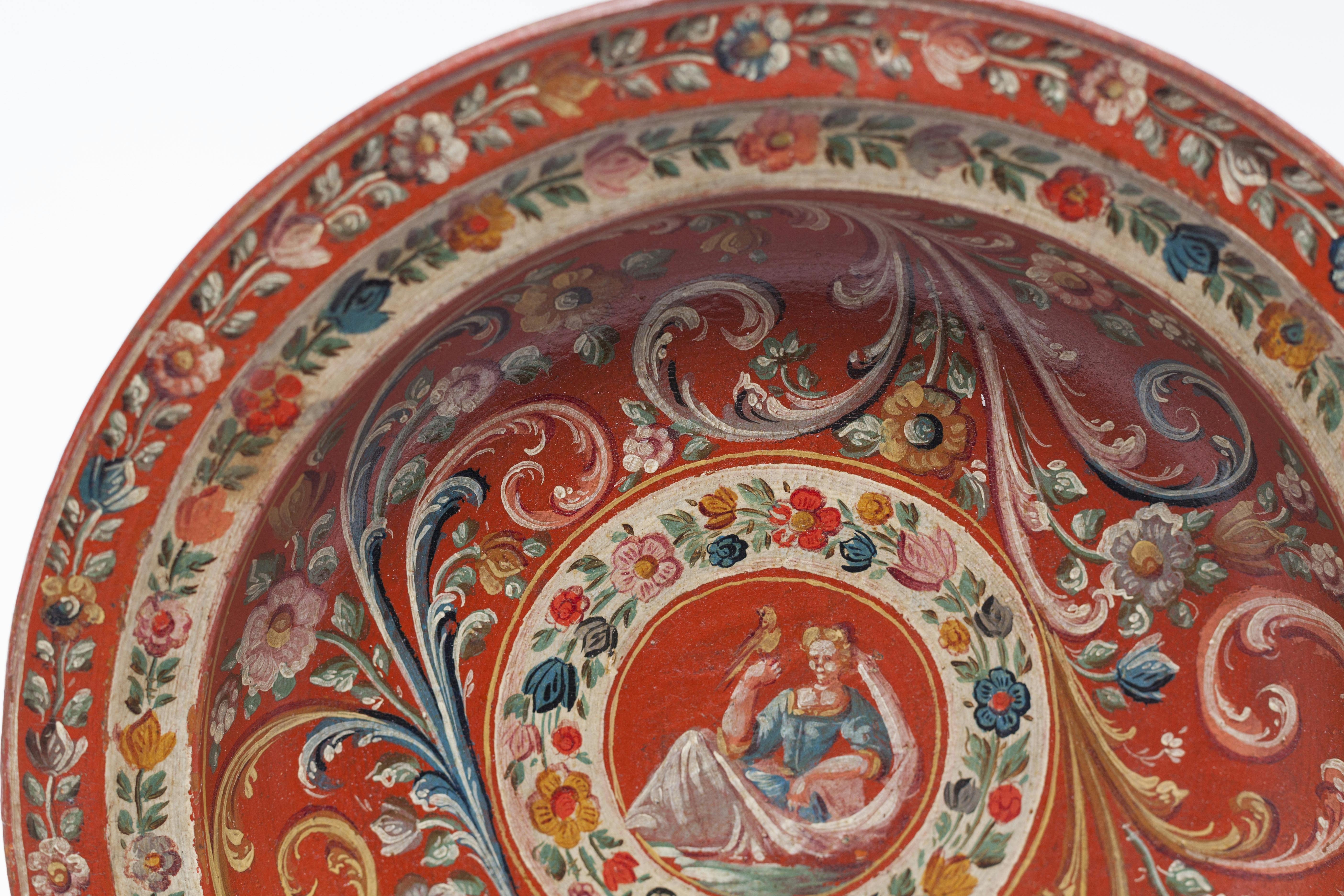 Ornate, red plate with intricate floral patterns and a central depiction of a seated figure surrounded by flowers.