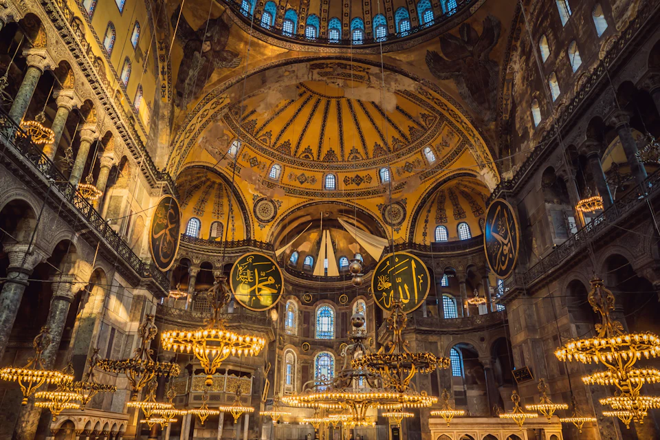 Interior view of a grand domed building with intricate decorations, chandeliers, and Arabic calligraphy on circular panels.