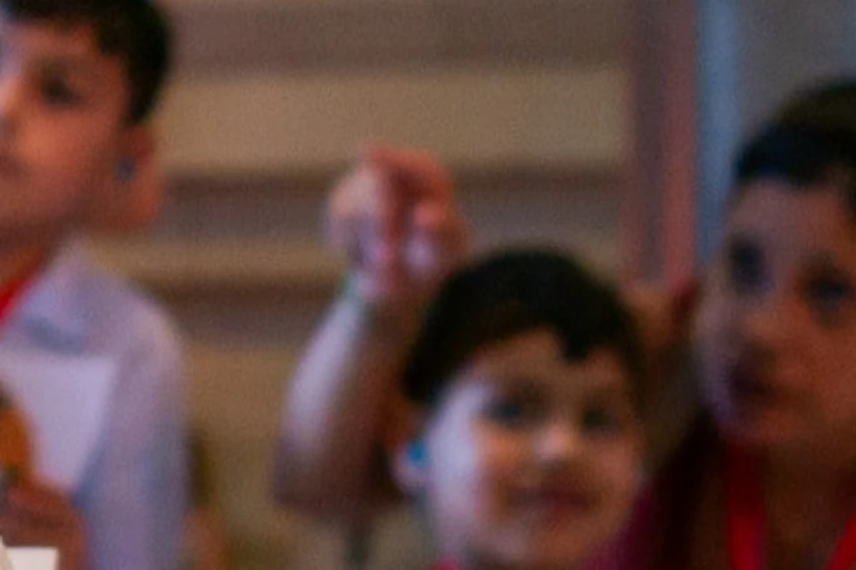 Children and adults with red lanyards inside a building with colorful stained glass windows.